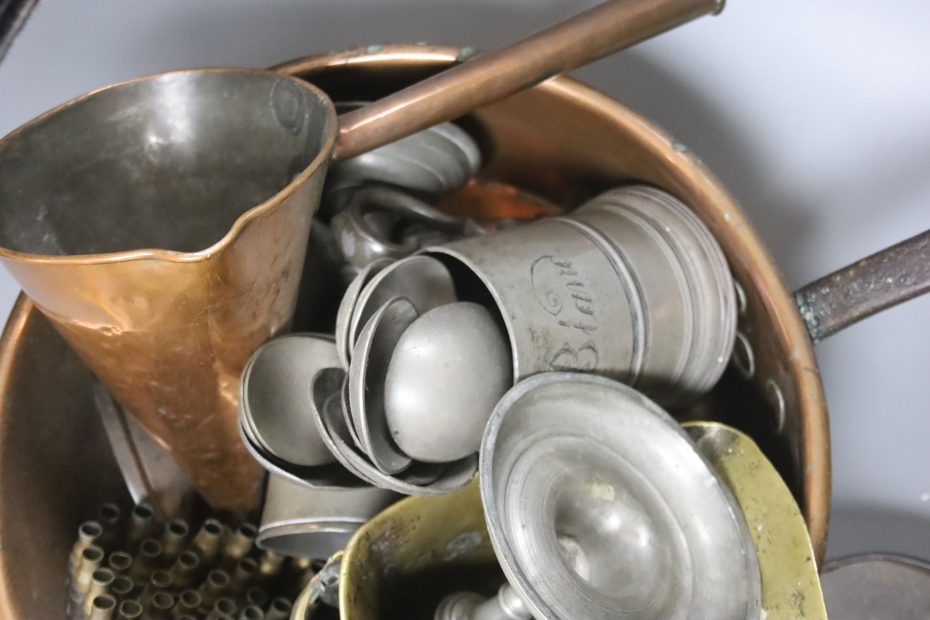 A group of assorted metalware including a copper pan, a brass stirrup, a pewter mug filled with pewter spoons, and a pair of toleware coasters